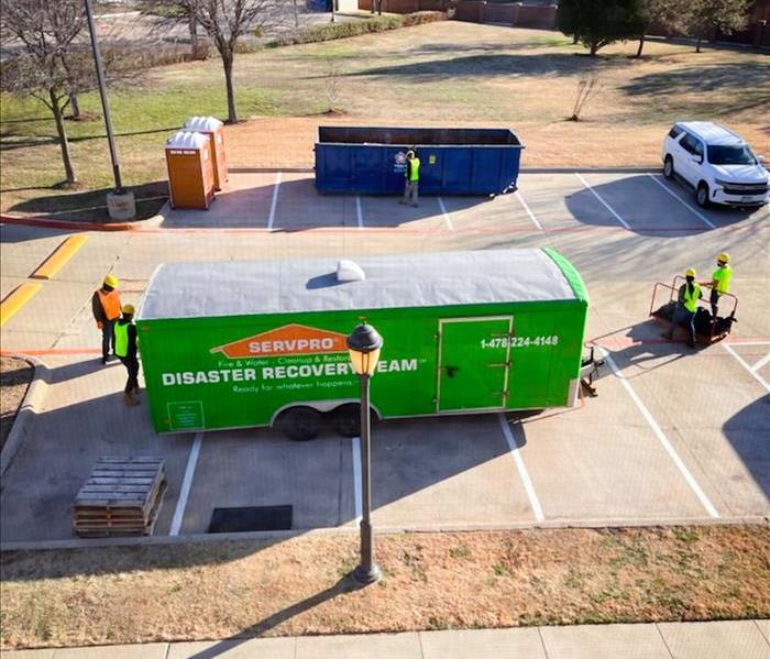 SERVPRO green Disaster Recovery truck trailer parked outside of a property restoration project with four workers around it. 